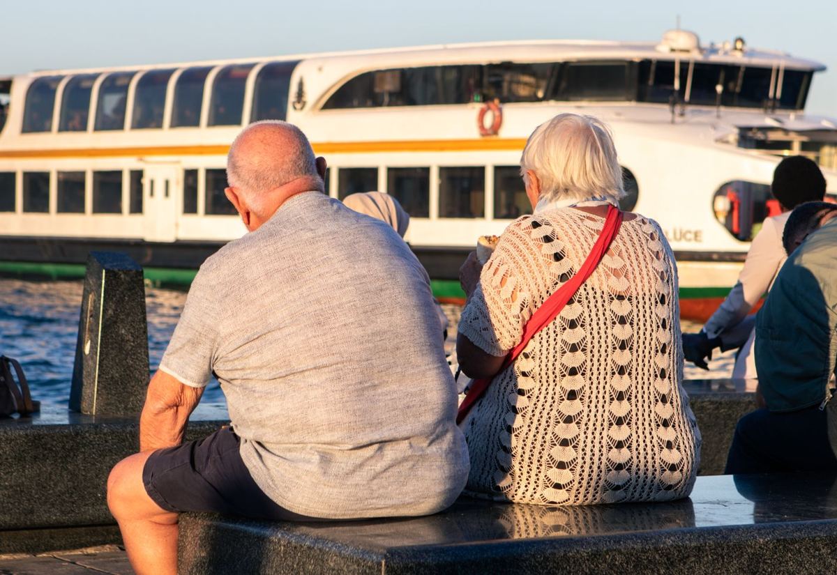 Casal de idosos sentado à beira-mar, visto de costas